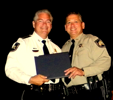 Sheriff Pohlmann, on stage for the ceremonies, presrnts Deputy Eric Eilers his certificate. 