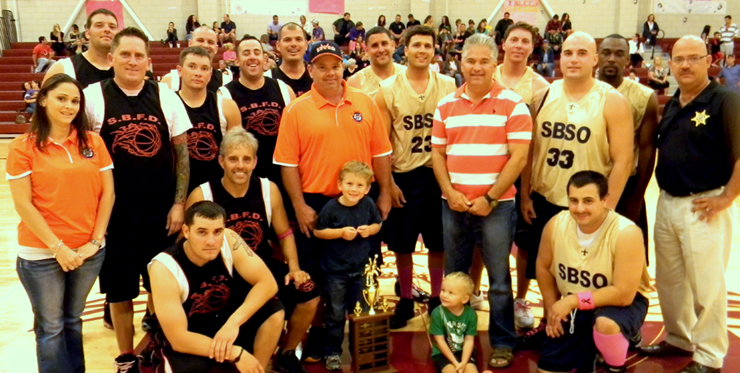 Both teams are shown after the trophy presentation. At left is Amanda Mones, representing corporate sponsor Gulf Coast Bank; from the Fire Department team are, kneeling, Wayne Letort and Mike Dragon; standing from left Joey Dullary, Daniel Dubose, Nick Elfensohn, back row, Mike Wolfe, Craig Miller, Brad Tregle; standing in middle is St. Bernard Youth Booster Club head Dwayne Gref and his son Gavin; and from the Sheriff's Office team at right, kneeling, are Brayden Nuccio, son of Deputy Brad Nuccio, and Justin Topey; standing are Sheriff James Pohlmann, Brad Nuccio and Coach Col. David Mowers; and in back from the Sheriff's Office are Jonathan Smith, Ryan Laylle, Brandon Licciardi and Shelton Smith.