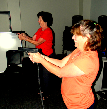 Karen Coombs of Arabi, in the foreground, and Terri Guate of St. Bernard, in the background, point their guns at a screen that will show them computerized videos and call for them to decide whether to shoot a criminal  suspect in the firearms simulator program.