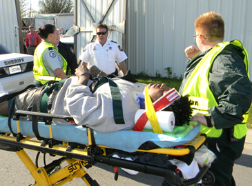 Torraino Johnson is shown on a gurney with emrgency medical technicians Robyn Penick, left, and April Wensel, right, both of Acadian Amlulance Srvices, who are about to take him to an ambulance. In the background is Maj. Robert McNab, head of the Criminal Investigations Bureau of the Sheriff's Office.