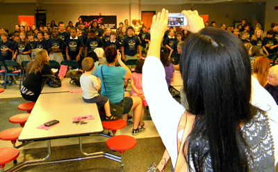 Wilma Oliveira, mother of student Ciao Oliveira, videos the graduates as they stand toward their parents and sing the D.A.R.E. theme song. 