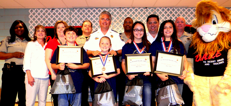 At Our Lady of prompt Succor School, from left are Lt. Lisa Jackson, teachers Anne Fabian and Rachel Vogt, 2nd place D.A.R.E. essay winners Joey Bazile and Katie Mahler; first place essay winners Emily Zepeda and Kelsey Juan, Sgt. Darrin Miller, Sheriff James Pohlmann, Lt. Richard Jackson, Maj. Chad Clark, Capt. Ronnie Martin and mascot Daren the Lion, portrayed by Cpl. Jessica Gernados.