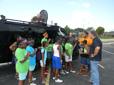 Sheriff Pohlmann, and to his right Rev. Henry Ballard of Christian Fellowship which sponsored the summer camp, talk to participants next to the sheriff's SWAT truck.