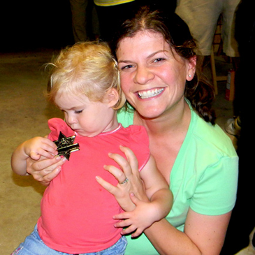 Emily Hanson holds her daughter, Elizabeth, age two, who is looking down to examine her Junior Deputy badge she just received at a Night Out Against Crime party in Meraux.