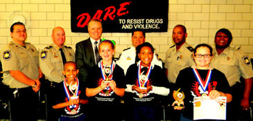 At Arabi Elementary School. in the front row are D.A.R.E. essay winners, from left, Darrell Williams Jr., Olivia Chaupette. Jaila Day and Livia Deane; in back are Sgt. Darrin Miller, Capt. Ronnie Martin, Chief Deputy Sheriff Richard Baumy, Maj. chad Clark, Lt. Richard Jackson and Lt. Lisa Jackson.