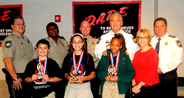 At Joseph Davies Elementary, essay winners are, from left, Kaleb Larousse, Michele Wilson and Da' Shyrah Sims. The fourth winner, Emily Brand, wasn't present. On the right is Principal Donna Schultz. In back are Sgt. Darrin Miller, Lt. Lisa Jackson, Sheriff James Pohlmann and Maj. Chad Clark.