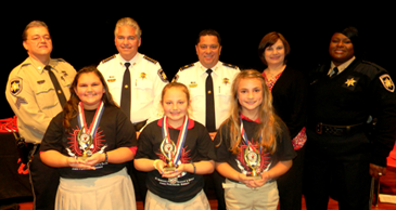 At J.F. Gauthier Elementary School, essay winners are, from left, Zoe' Latapie, Isabella Bazile and Camille Thomassie; in back are Sgt. Darrin Miller, Sheriff James Pohlmann. Maj. Chad Clark, Principal Lisa Young and Lt. Lisa Jackson.