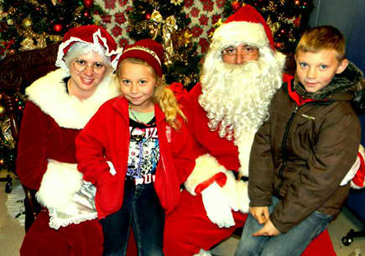 Visiting with Santa and Mrs. Claus at the Santa on the Bayou toy distribution are, at left, Daylen McNeill being held by Mrs. Claus, portrayed by Jessica Naquin, and Alden McNeill, being held by Santa, portrayed by Darrall Monk. 