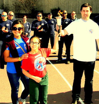 Alexis Hernandez, 12, of Arabi Elementary, center, holds the Special Olympics torch aloft with the help of Gerald Neyland of Arabi, with her older sister Elizabeth Hernandez, at left and a group of St. Bernard Parish sheriff's deputies behind them as they get ready to march in the opening ceremony of the school system's Special Olympics games held March 14 at Chalmette High's football stadium. Alexis, a eunner, will compte in the national Special Olympics in June at Princeton, N.J.
