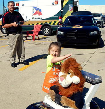 Catherine O'Neill of Arabi pets the head of Daren the Lion, mascot of the D.A.R.E. drug resistance education program taught in schools by the Sheriff's Office. In the background operating the remote control car is Sgt. Darrin Miller of the D.A.R.E. program.